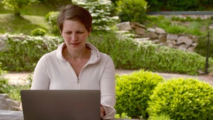 Barbara Pachl-Eberhart sitzt mit einem Laptop an einem Tisch in einem Garten.