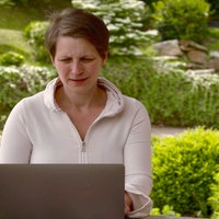 Barbara Pachl-Eberhart sitzt mit einem Laptop an einem Tisch in einem Garten.