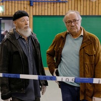 Zwei Männer stehen hinter einem Polizeiabsperrband in einer Sporthalle