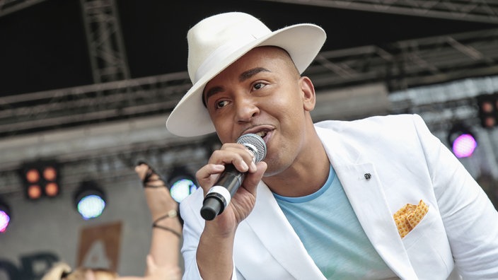 Sänger Lou Bega mit einem Mikrofon in der Hand.