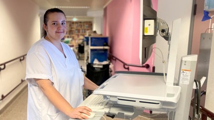 Eine Krankenschwester steht in einem Flur vor ihr ein Computer.