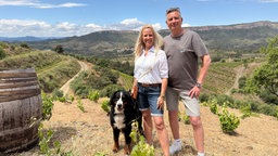 Sandra und Klaus stehen mit Ihrem Hund vor einer Berglandschaft.