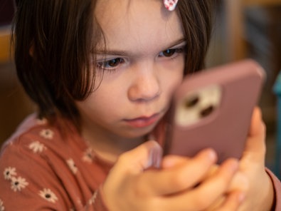 Ein Kind sitzt am Küchentisch und richtet seine ganze Aufmarksamkeit auf ein Smartphone.
