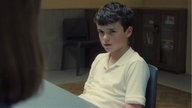 Szene aus der britischen Netflix-Serie "Adolescence": Junge in weißem T-Shirt sitzt an einem Tisch