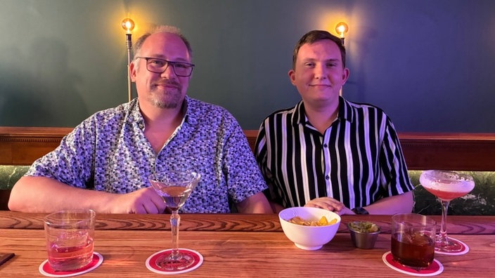 Zwei Personen sitzen an einem Tisch und vor ihnen stehen mehrere Coktails