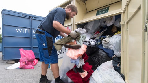 Ein Mann sortiert Kleidung aus einem Altkleidercontainer