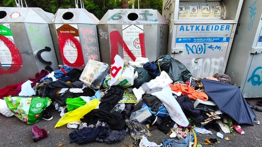 Verschiedener Müll und Altkleider liegen vor den Container für Altglas und Altkleider