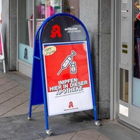 Eine Apotheke mit einem Aufsteller vor dem Eingang, der auf die Möglichkeit einer Grippeschutzimpfung hinweist