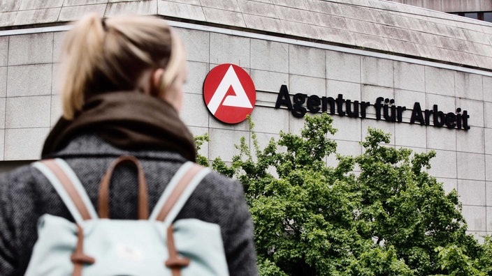 Eine junge Frau schaut auf das Schild der Bundesagentur für Arbeit