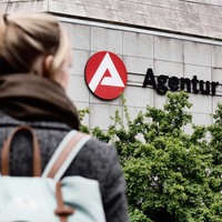 Eine junge Frau schaut auf das Schild der Bundesagentur für Arbeit