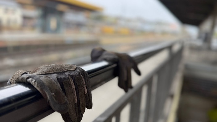 Auf einem Geländer an einem Bahnsteig leigt ein Paar Arbeitshandschuhe