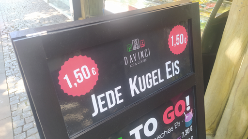 Ein Aufsteller mit der Aufschrift "Jede Kugel Eis 1,50€" steht vor einer Eisdiele 