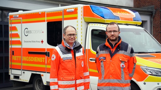 Christoph Schlütermann und Sven Nolte stehen vor einem Rettungswagen der Wache Coesfeld