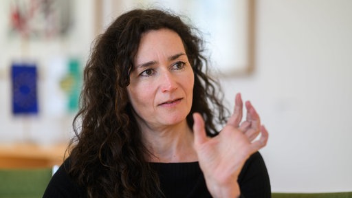 Eine Frau mit braunen, lockigen Haaren gestikuliert mit ihrer Hand