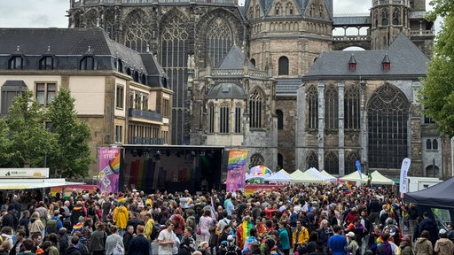 Besuchende des CSD in Aachen stehen vor einer Tribüne