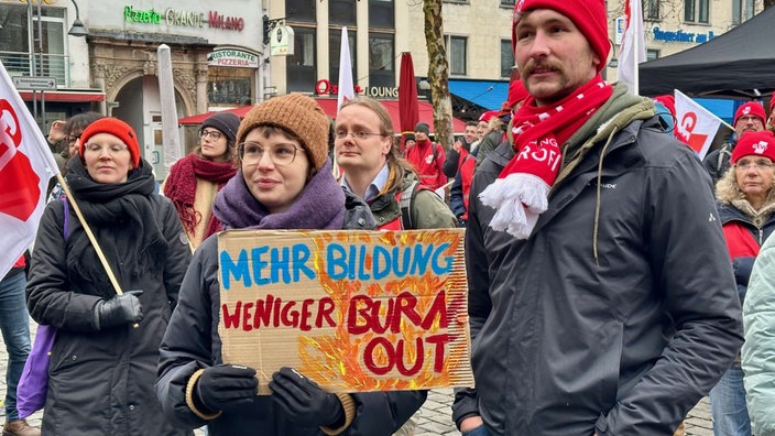 Eine Frau hält ein Schild mit der Aufschrift: "Mehr Bildung, weniger Burn Out"