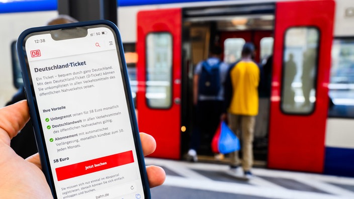 Am Bahnhof zeigt eine Person ihr Deutschlandticket auf dem Display eines Smartphones 