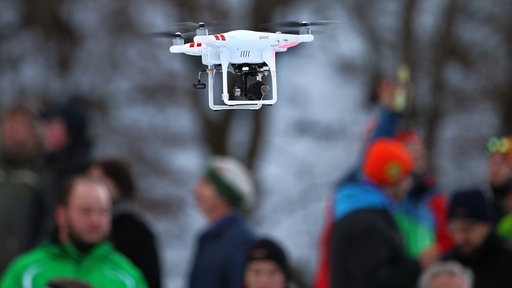 Eine mit einer Kamera bestückte Drohne fliegt über Zuschauer
