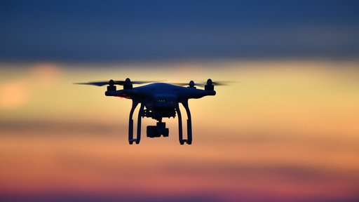  Eine Drohne fliegt bei Sonnenuntergang über eine Wiese