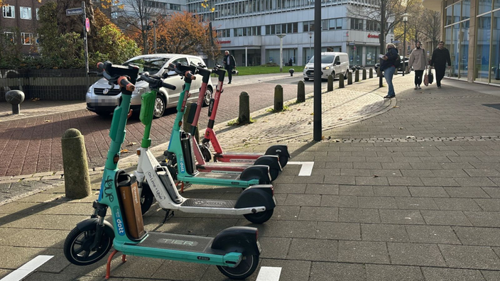 Mehrere E-Scooter stehen in einer Reihe in einer ausgewiesenen Zone.