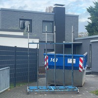 An einem Einfamilienhaus in Köln-Rodenkirchen sind Spuren des SEK-Einsatzes vom Juli noch sichtbar. Ein Container steht in der Einfahrt, der beschädigte Treppenabsatz wird repariert.