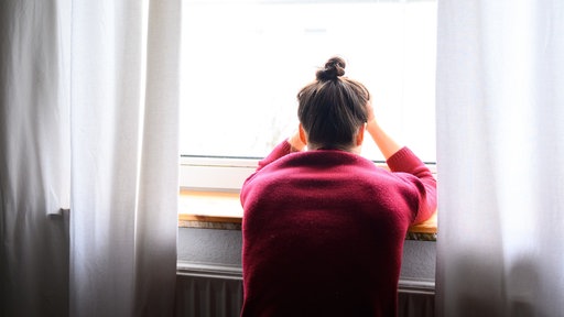 Eine Frau sitzt mit Kopf in den Händen einsam am Fenster