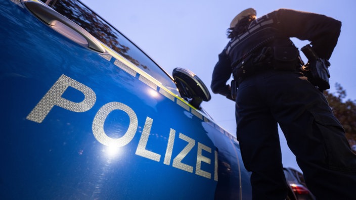 Eine Polizisten steht vor einem Polizeiauto
