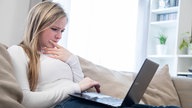 Eine Frau schaut nachdenklich auf ihren Laptop 