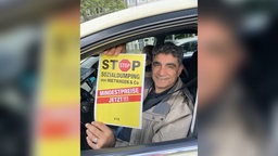 Taxifahrer sitzt in Auto und hält Schild hoch
