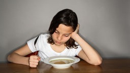 Ein Mädchen sitzt lustlos vor einem Teller Suppe