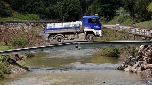 Ein blauer LKW fährt über eine provisorische Brücke, links und rechts liegt Schutt.