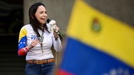 Friedensnobelpreisträgerin Maria Corina Machado auf einer Protestveranstaltung in Caracas am 9. Januar 2025 mit einer unscharfen Venezuela-Flagge im Vordergrund