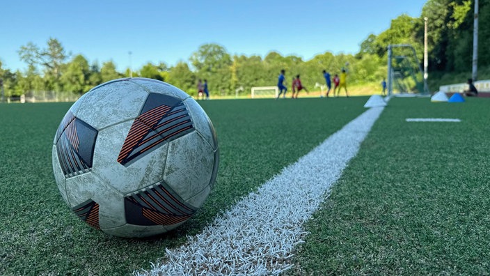 Fußball im Vordergrund - Jugendspiel im Hintergrund