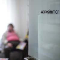 Eine milchige Glastür mit der Aufschrift "Wartezimmer" gibt den Blick auf drei verschwommene Patienten