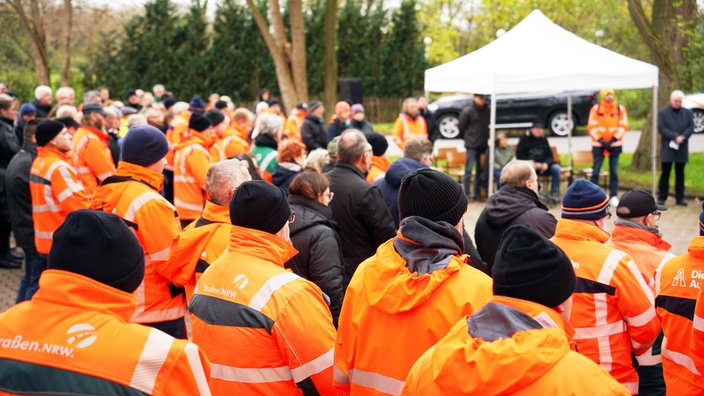 Hunderte Straßenwärter stehen gemeinsam mit roten Warnwesten vor der Gedenkstätte