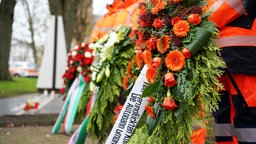 Straßenwärter mit Krenzen vor der stählernen Gedenkstätte