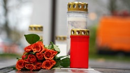 Blumen liegen neben Kerzen vor der stählernen Gedenktafel