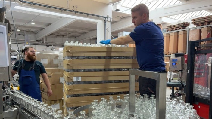 Zwei Arbeiter stehen in der Produktion neben Glasflaschen auf einem Fließband
