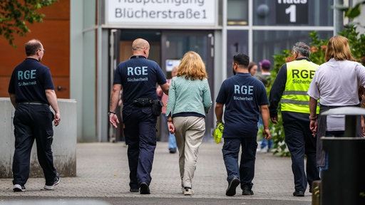 Mehrere Mitarbeiter der Schule und eines Sicherheitsunternehmens gehen auf dem Gelände der Schule, in der ein Angriff auf eine Lehrerin stattgefunden hat. 