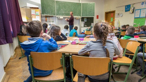Der Grundschullehrer erklärt eine Rechenaufgabe an der Tafel. 