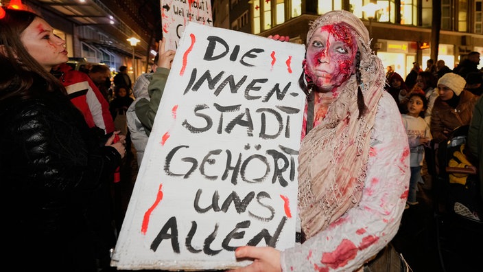 Person verkleidet als Zombie hält ein Schild mit der Aufschrift:  "Die Innenstadt gehört uns allen" 