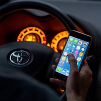Ein Mann sitzt in einem Auto am Steuer und hält ein Smartphone in der Hand