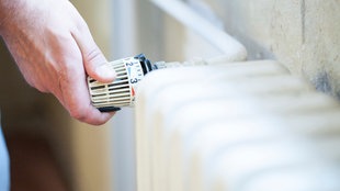 Eine Hand dreht an einem Heizthermostat