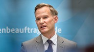Hendrik Streeck in einem grauen Anzug vor einem blauen Hintergrund