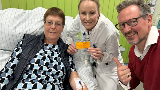 Ein Mann und eine Frau stehen neben einer älteren Dame am Krankenbett