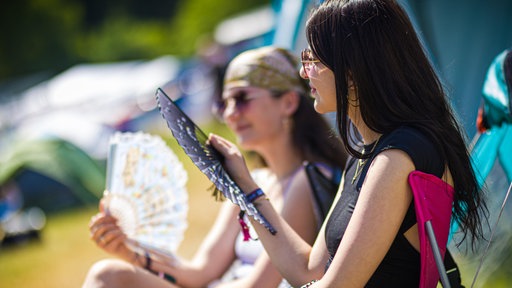 Zwei Frauen sitzen mit Fächern in der Hand in der Sonne 