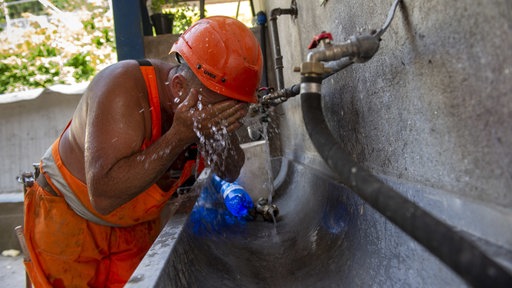 Ein Bauarbeiter einer Strassenbaustelle kühlt sich an einem Wasserhahn ab.