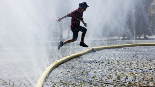 Ein Junge springt über einen Schlauch, aus dem Wasser spritzt, um sich gegen die Hitze abzukühlen.