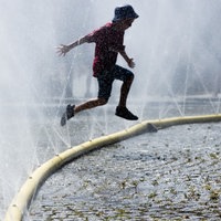 Ein Junge springt über einen Schlauch, aus dem Wasser spritzt, um sich gegen die Hitze abzukühlen.