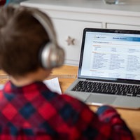 Ein Junge (von hinten) sitzt mit Kopfhörern vor seinem Laptop, auf dem ein Lernprogramm geöffnet ist.
